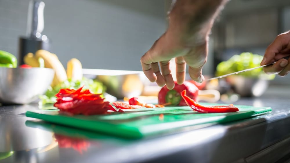 Hands slicing red bell pepper on a chopping board in a kitchen setting, ideal for culinary visuals.
