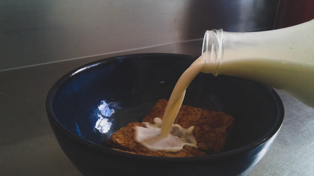 Close-up of milk being poured into a dark bowl with breakfast cereal, creating a calm morning scene.