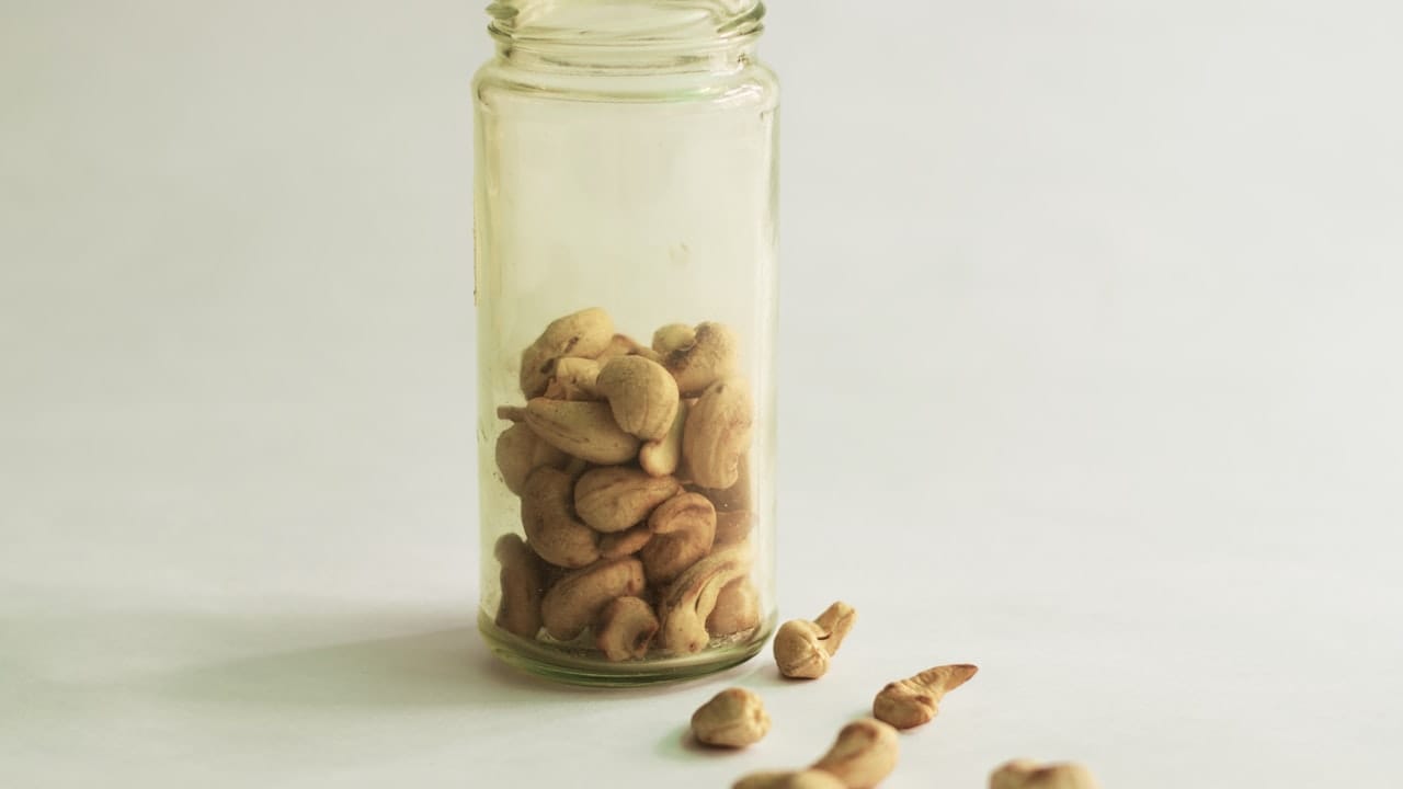 Cashew nuts in a glass jar and spilled on white.