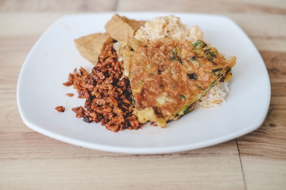 Close-up of vegetarian nasi campur dish on a white plate with tempeh and fritter.
