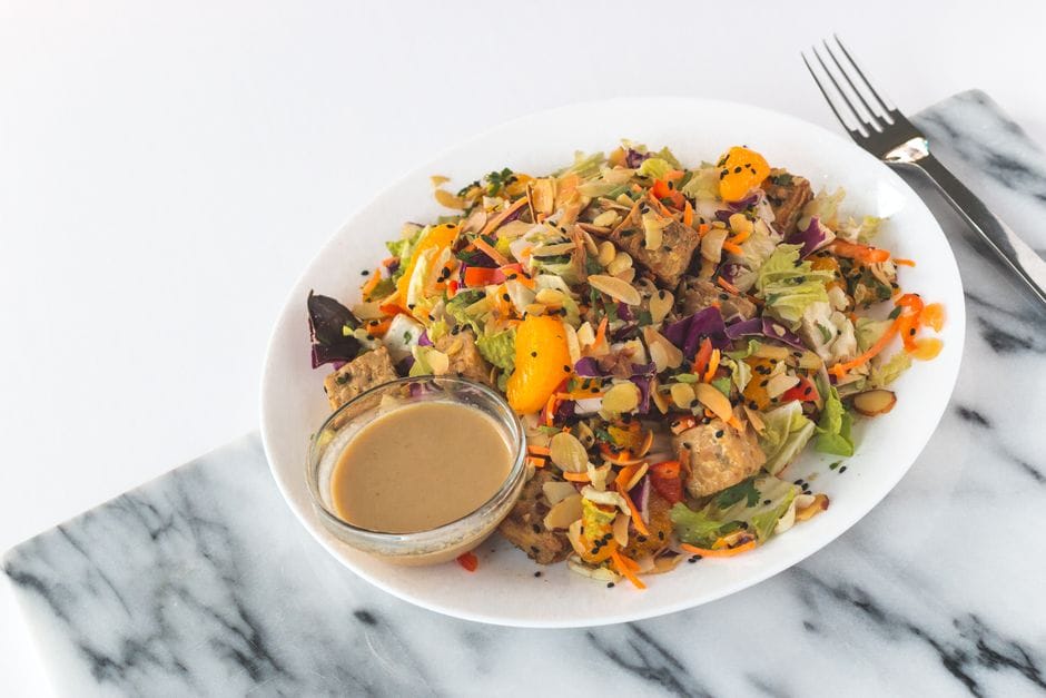 A vibrant mandarin almond salad featuring fresh veggies, tempeh, and a side of creamy dressing.