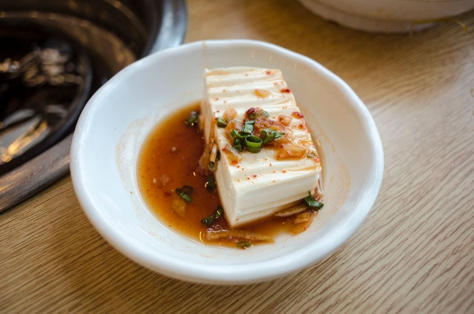 Close-up of tofu in spicy sauce garnished with green onions in a white bowl, perfect for food photography.