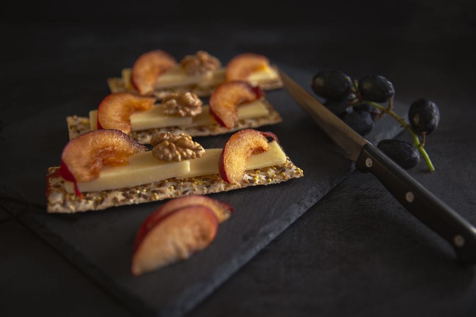 Appetizing cheese, peach, and walnut on crispbread on a slate surface.