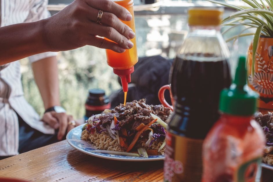 A person adding sauce to a street food meal on a wooden table.