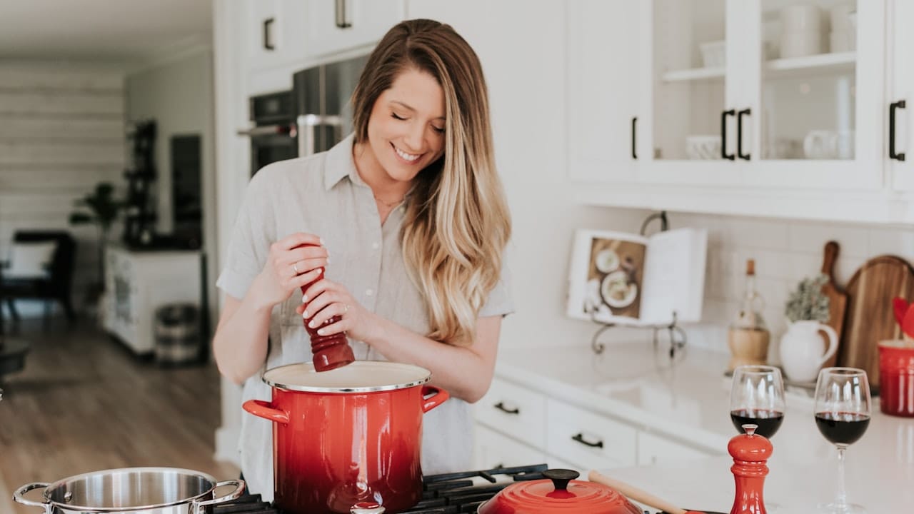 smiling woman standing and putting pepper on stock pot