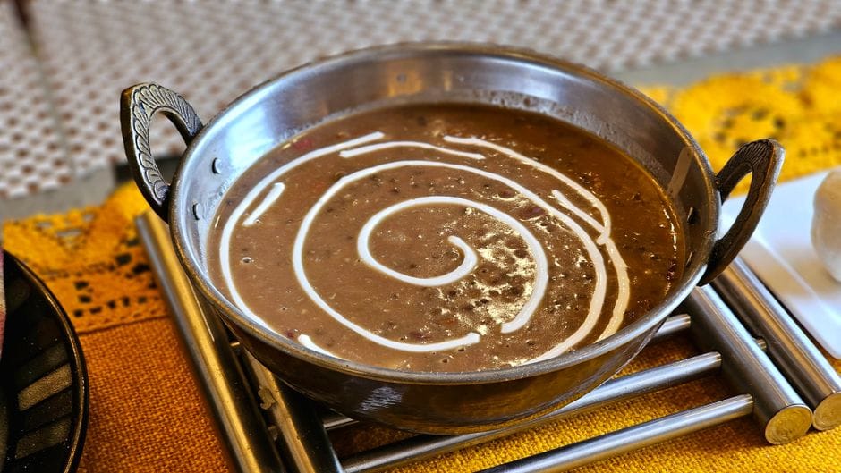 Creamy dal makhani garnished with cream served in a traditional metal bowl on a textured tablecloth.