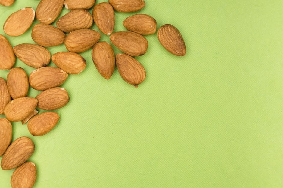 A close-up of almonds scattered on a vibrant green background with ample copy space.