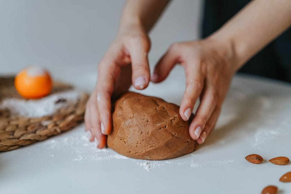 Hands kneading almond dough on a white table with flour and almonds around.