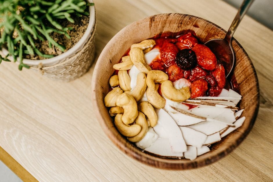 Healthy breakfast bowl with cashews, berries, and coconut slices in a wooden bowl.