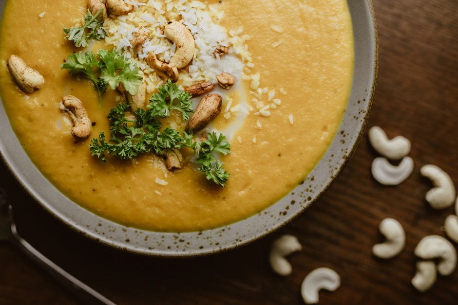 Delicious creamy pumpkin soup garnished with cashews and fresh herbs in a bowl.
