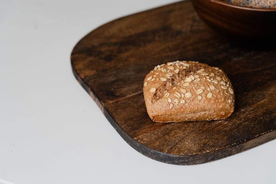 A freshly baked whole wheat bread roll with oats resting on a rustic wooden board.