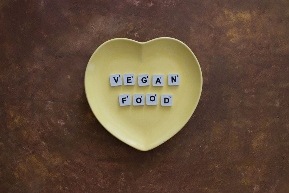 Yellow heart-shaped plate with scrabble tiles spelling 'vegan food' on a rustic background.
