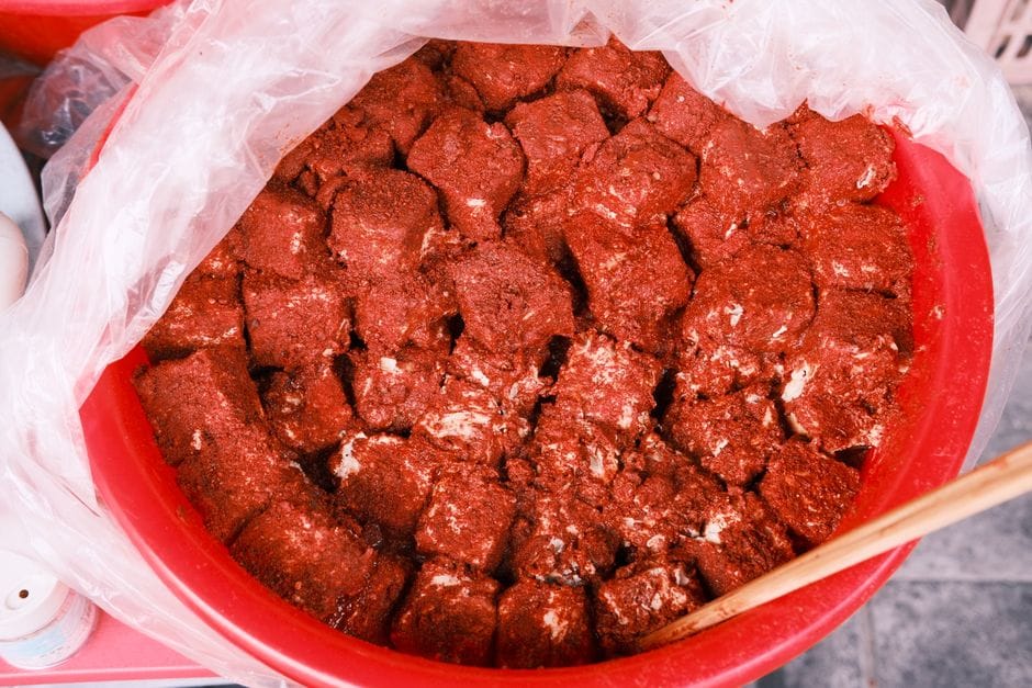 Freshly prepared spicy marinated tofu cubes in a red plastic bowl, ready to serve.