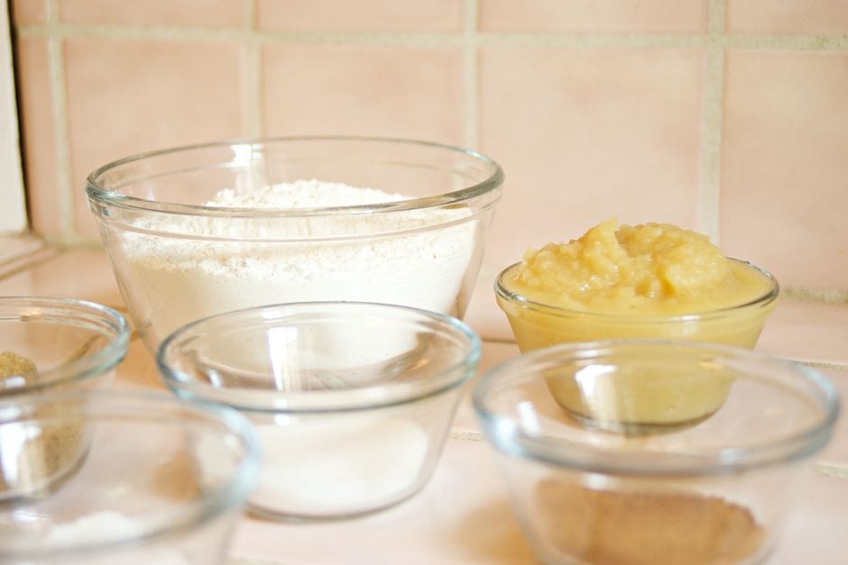 Close-up of glass bowls with flour, applesauce, and sugar, ready for baking.