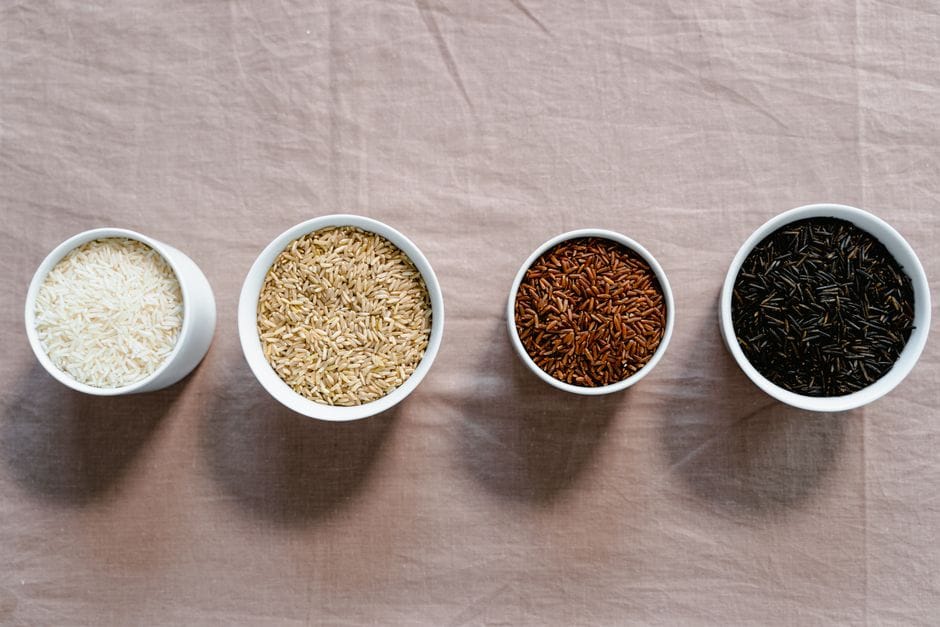 An overhead shot of different types of raw rice in bowls, placed in a row.