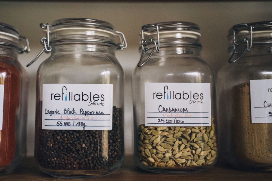 A collection of spices in eco-friendly refillable glass jars on a wooden shelf, promoting sustainable food storage.