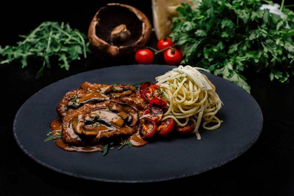 Delicious veal scaloppini with mushroom sauce and pasta, garnished with fresh herbs.
