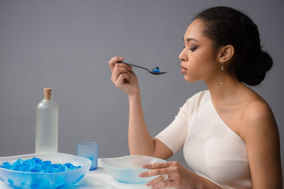 Woman elegantly savoring blue gelatin dessert in studio, exuding grace and style.