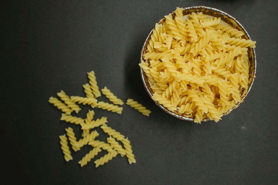 Top view pile of uncooked fusilli pasta twisted into springs in bowl and scattered macaroni placed on black background in kitchen