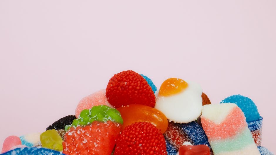 Close-up of assorted gummy candies with sugar coating on a pastel pink background.