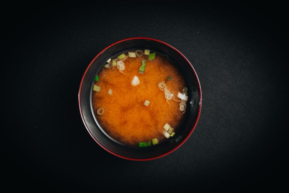 Top view of traditional miso soup with green onions and tofu in a black bowl on a dark background.