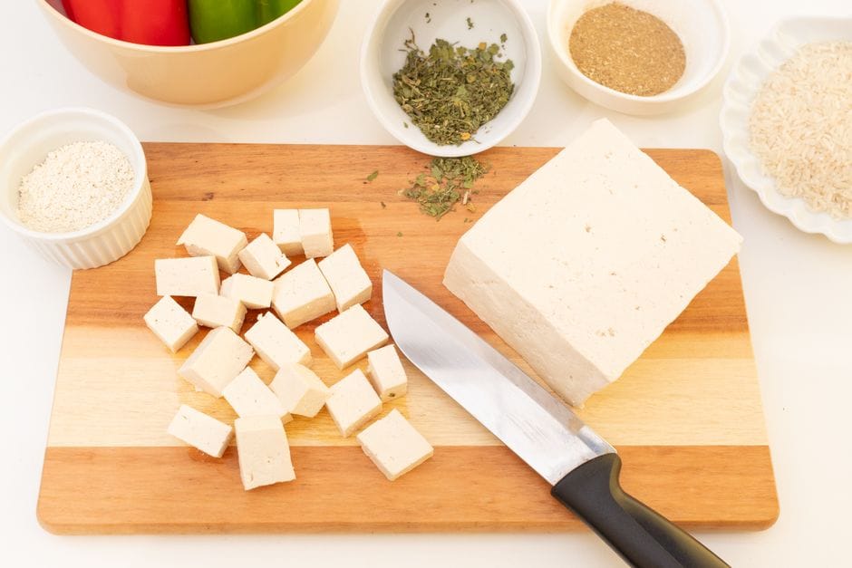 Sliced tofu on cutting board with herbs and spices, perfect for vegan meal ideas.