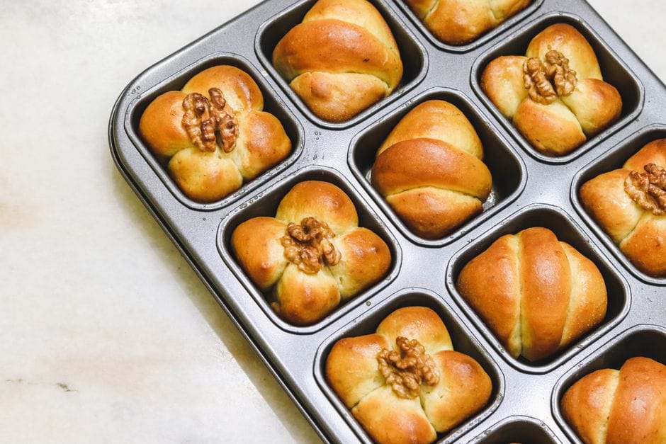 Top view of golden brown walnut-topped bread rolls in a baking tray on a marble surface.