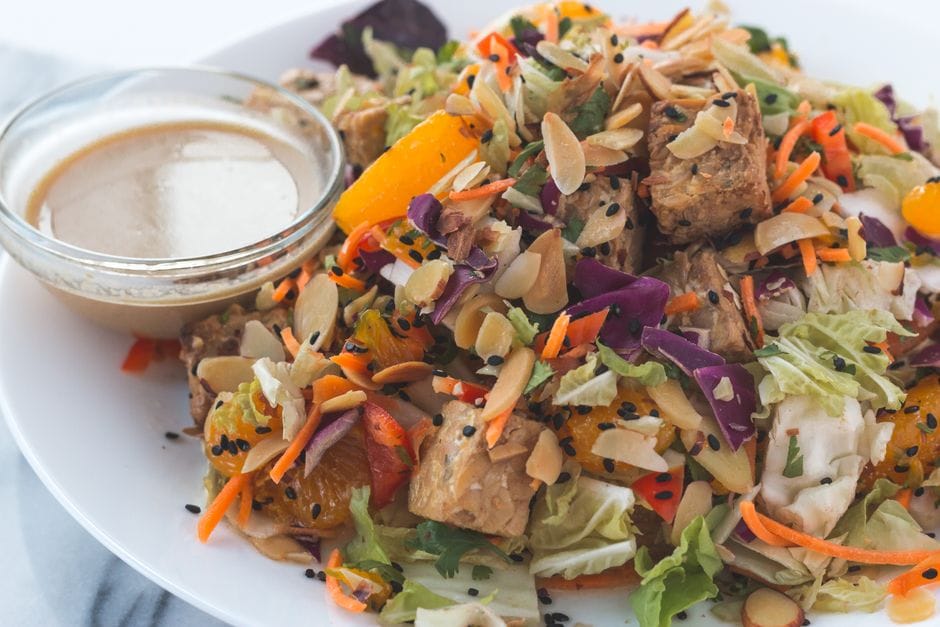 A vibrant vegan salad with tempeh, orange slices, and almonds served with dressing.