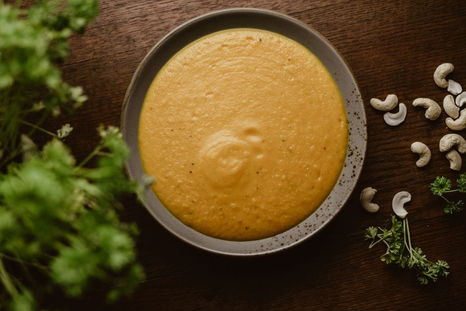A warm plate of creamy cashew soup garnished with fresh herbs, perfect for a vegan meal.