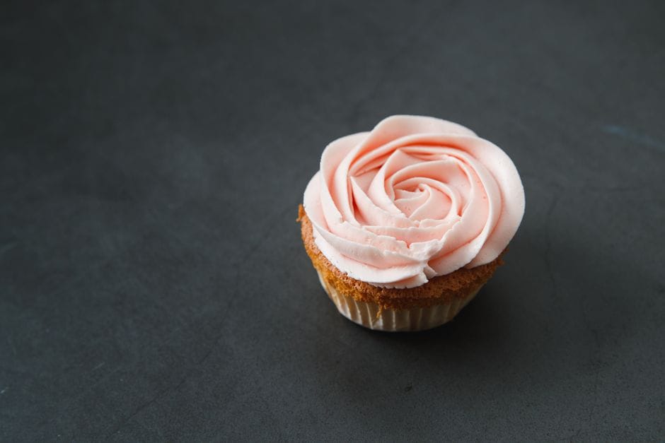 Delicate cupcake with rose-shaped buttercream frosting on a dark surface, perfect for dessert and bakery themes.