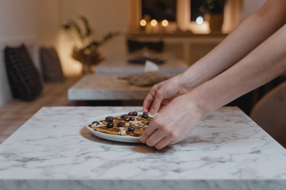 Hands arranging vegan pancakes with berries on a marble table in a cozy dining setting.