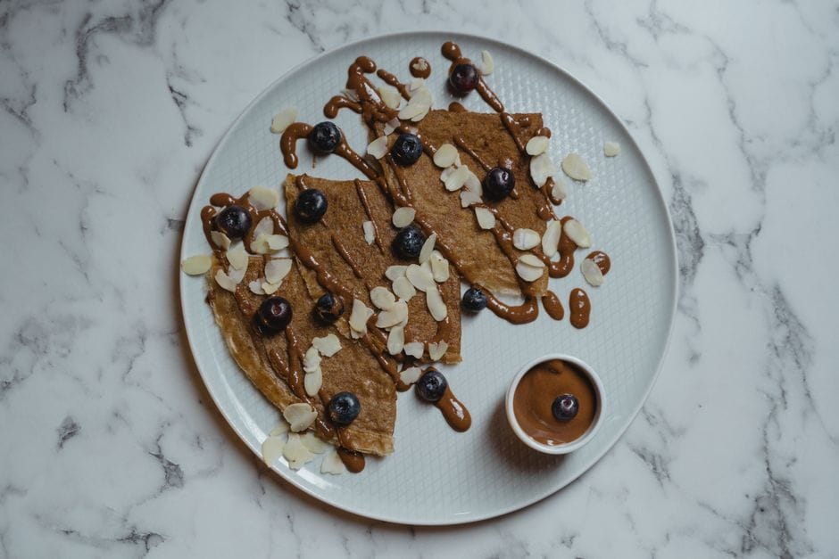 Delicious crepes topped with blueberries and almond slices, drizzled with chocolate sauce on a marble surface.