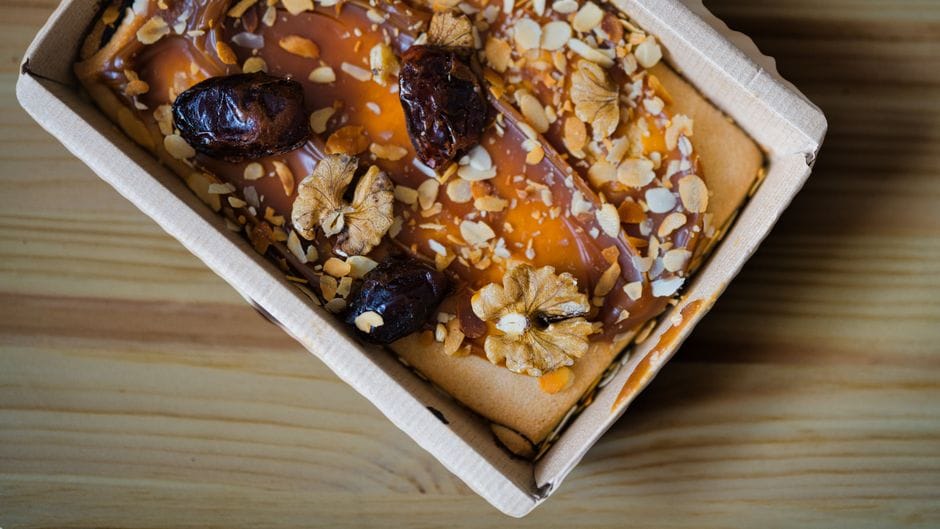 Top view of a date and nut cake with almonds and caramel in a paper box.