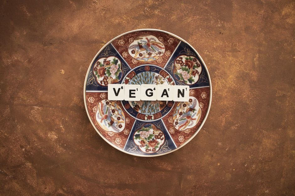 Artistic display of vegan text on a decorative plate against textured background.