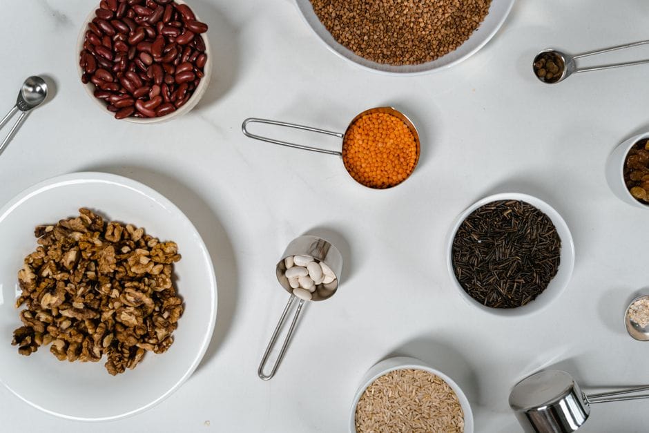 Flat lay of assorted grains, seeds, and nuts in bowls and cups on a white surface.
