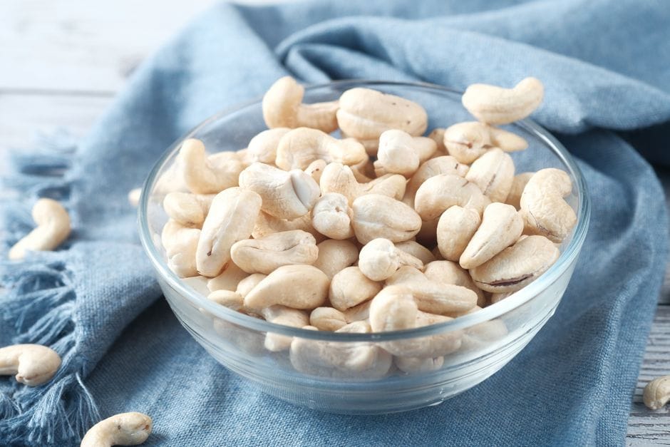A glass bowl filled with raw cashews on a blue cloth, perfect for healthy snacking.
