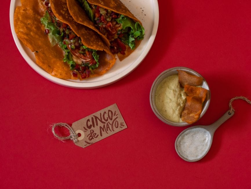 Delicious tacos and dips for a festive Cinco de Mayo celebration on vibrant red backdrop.