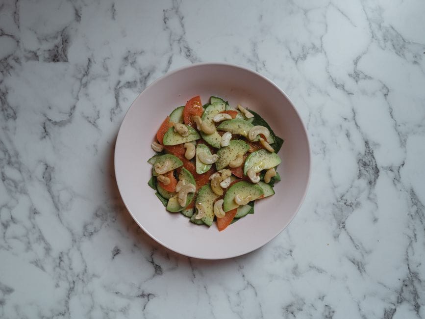 Delicious vegan salad with cucumbers, tomatoes, and nuts in a ceramic bowl.