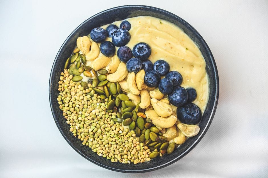 A fresh and nutritious breakfast bowl featuring blueberries, cashews, and seeds on a white surface.