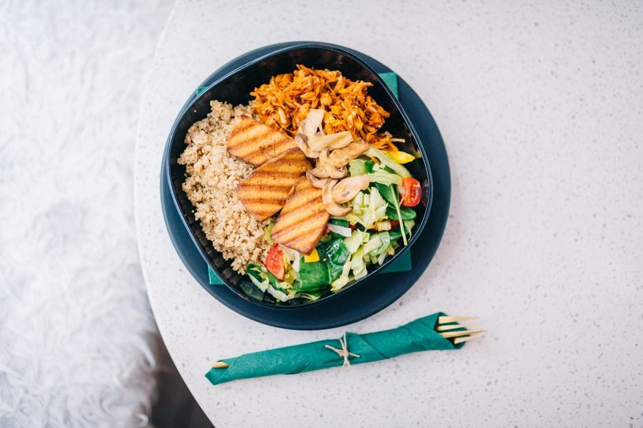 A nutritious bowl featuring grilled tofu, quinoa, fresh salad, and mushrooms on a light background.