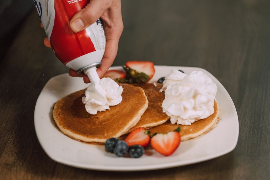 Close-up shot of pancakes with whipped cream, strawberries, and blueberries on a white plate.